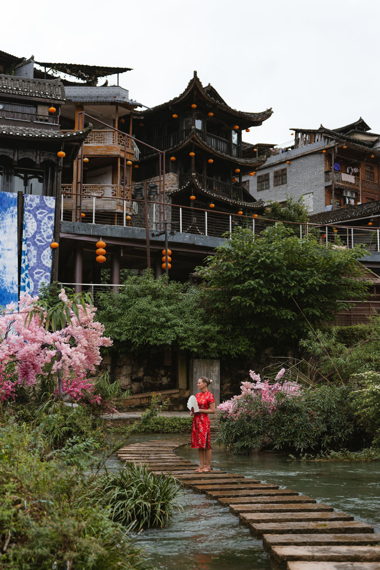 Woman in a red dress crossing stepping stones in Furong Ancient Town, China.