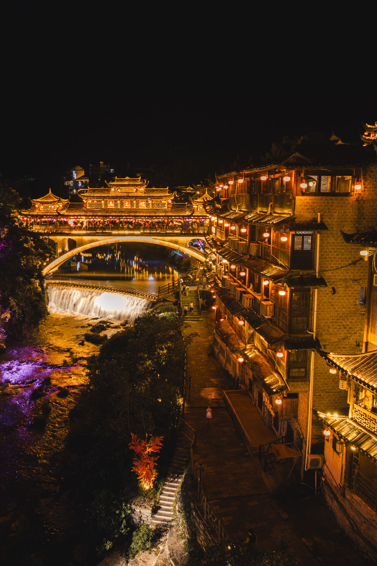 Furong Ancient Town bridge and traditional riverside buildings illuminated at night.