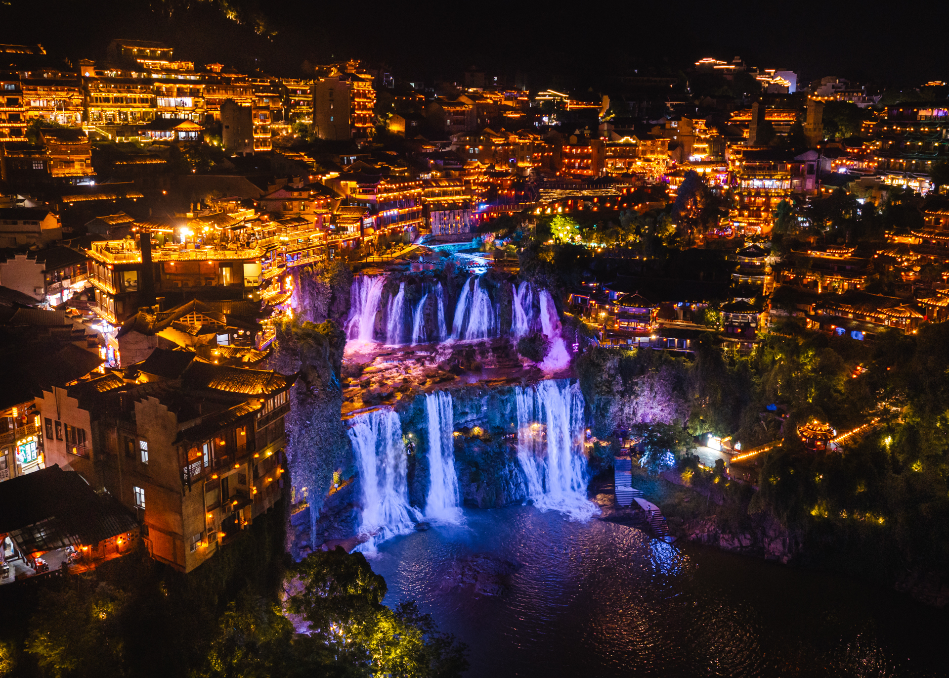 Furong Ancient Town illuminated at night with colorful waterfalls and traditional buildings.