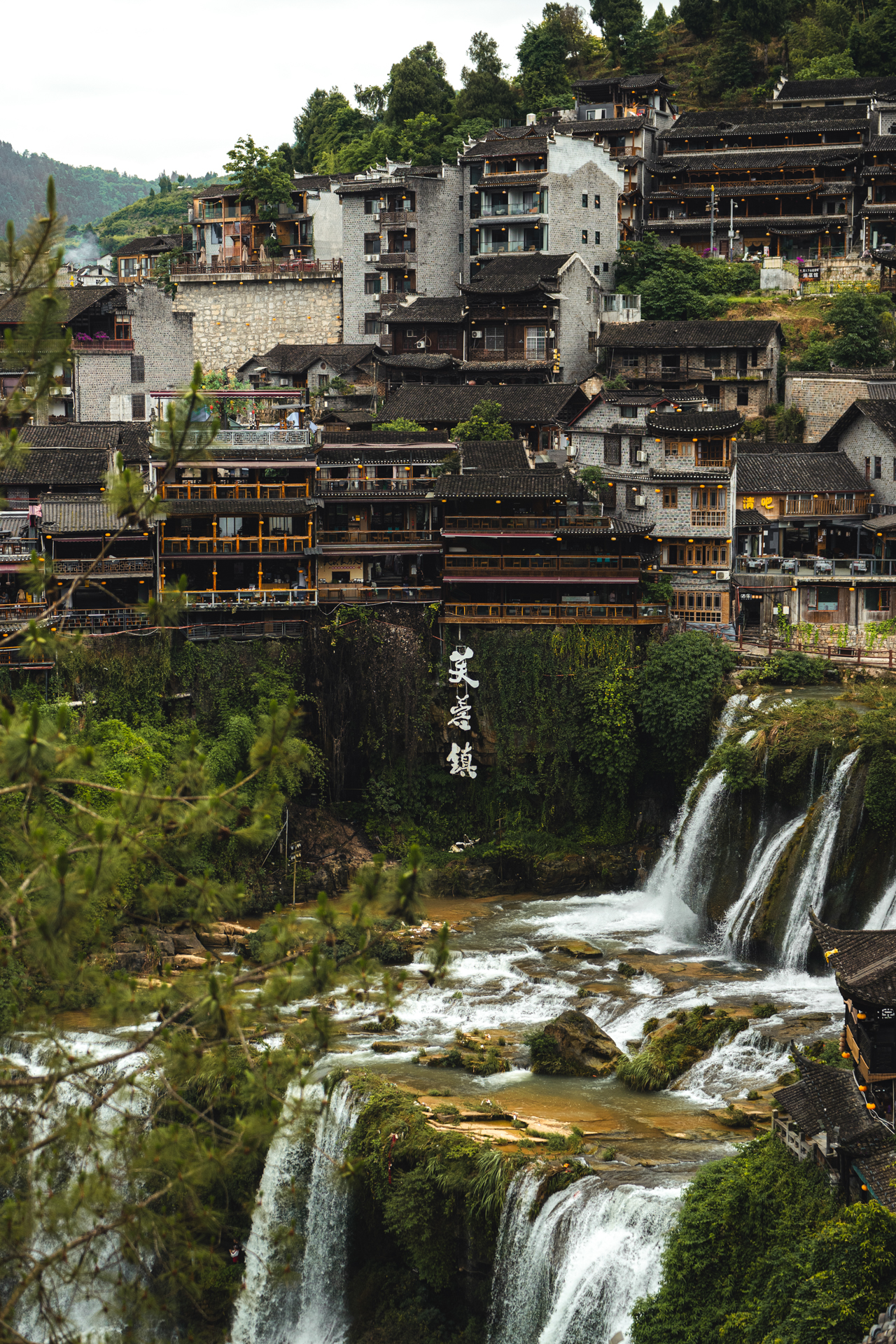 Furong Ancient Town built above cascading waterfalls and lush greenery in Hunan, China.