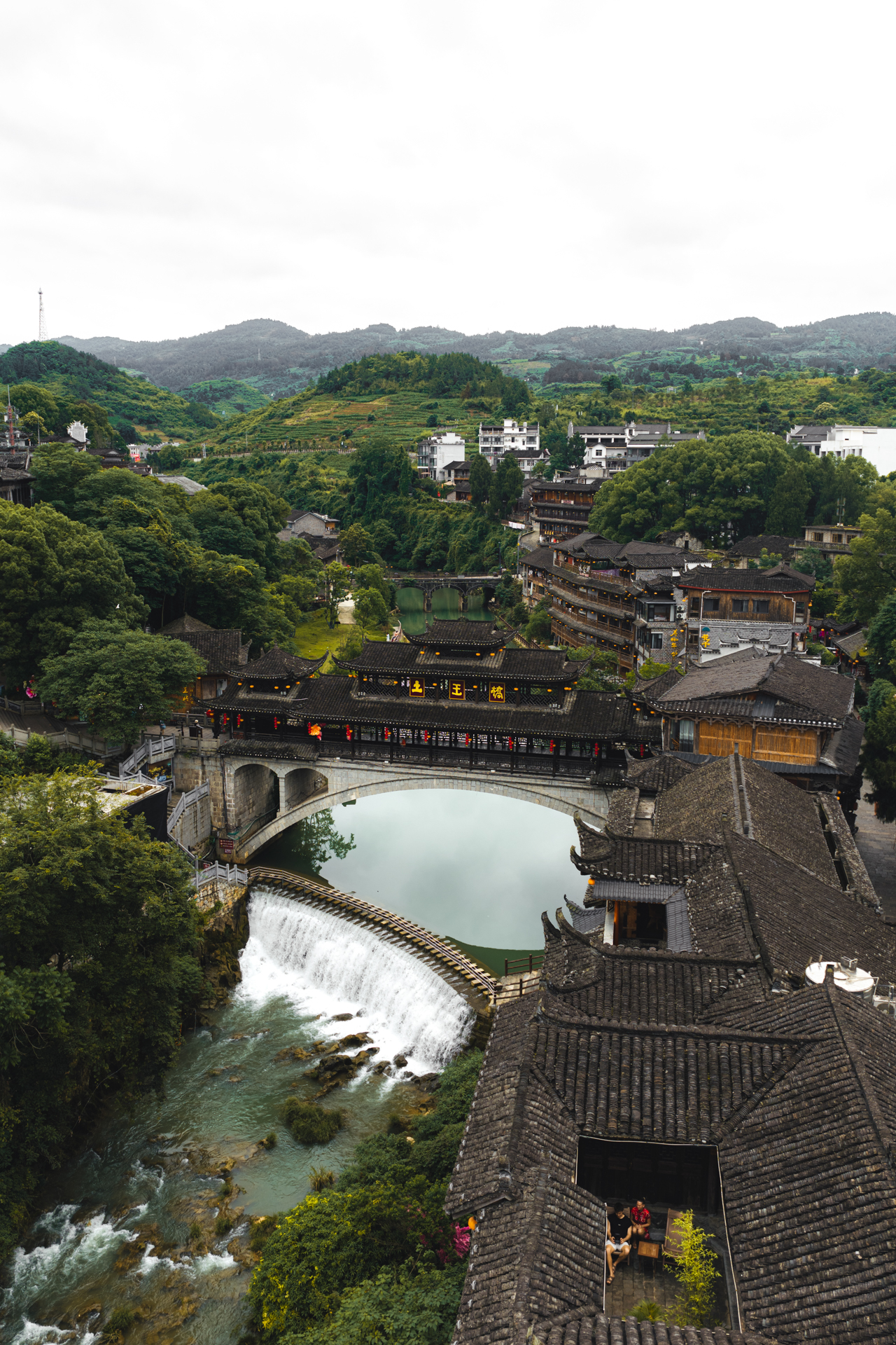 Aerial view of Furong Ancient Town bridge, waterfall and traditional rooftops in China.