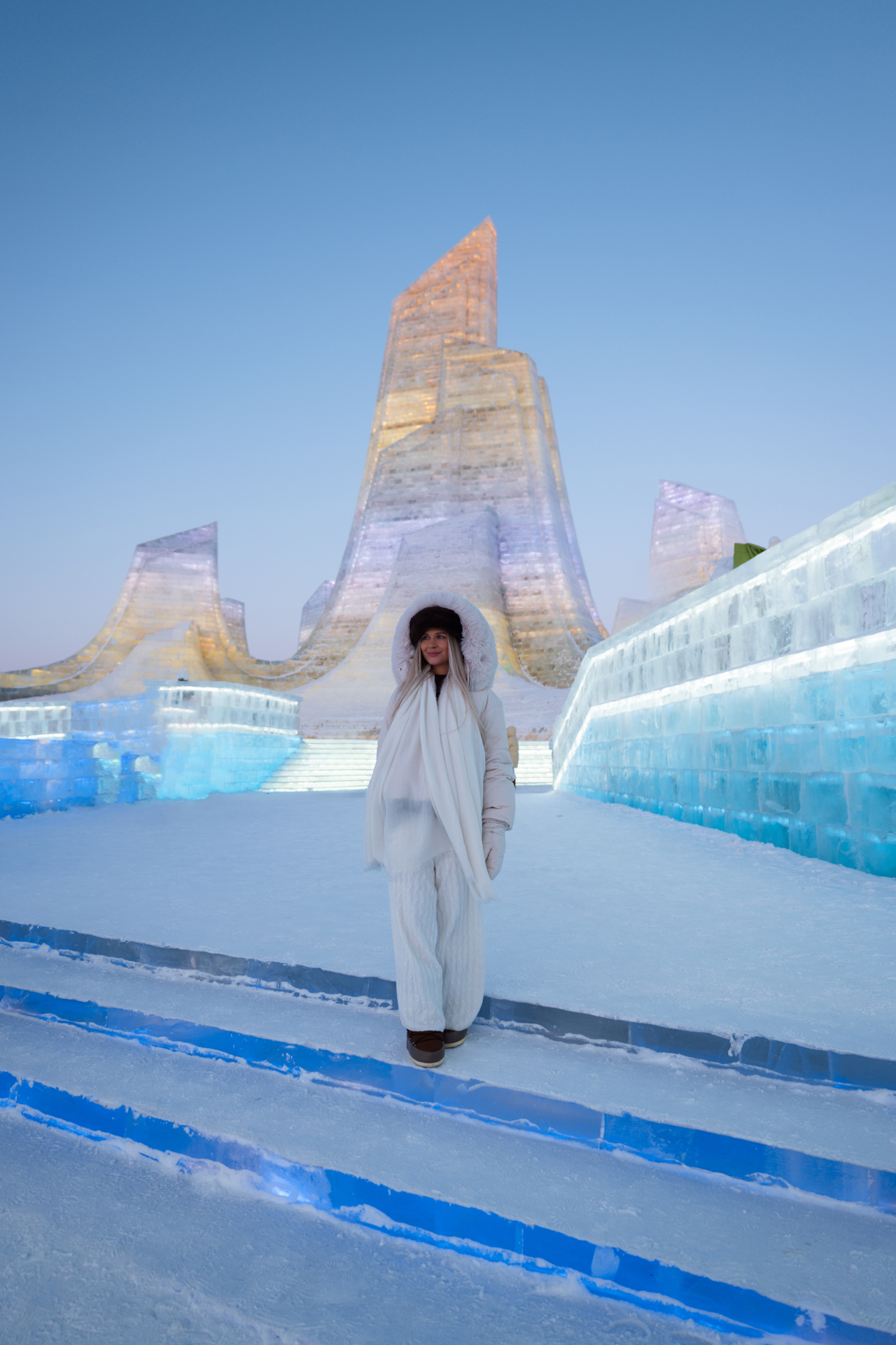 Woman standing among glowing ice sculptures at Harbin Ice and Snow World in China.