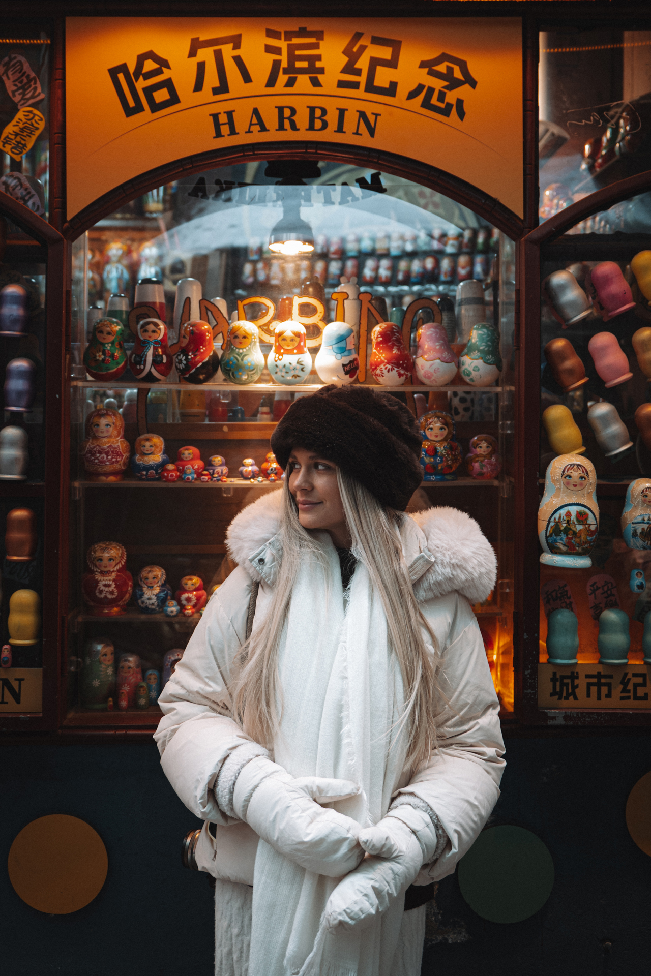Woman in winter clothing posing in front of colorful Russian nesting dolls in Harbin.
