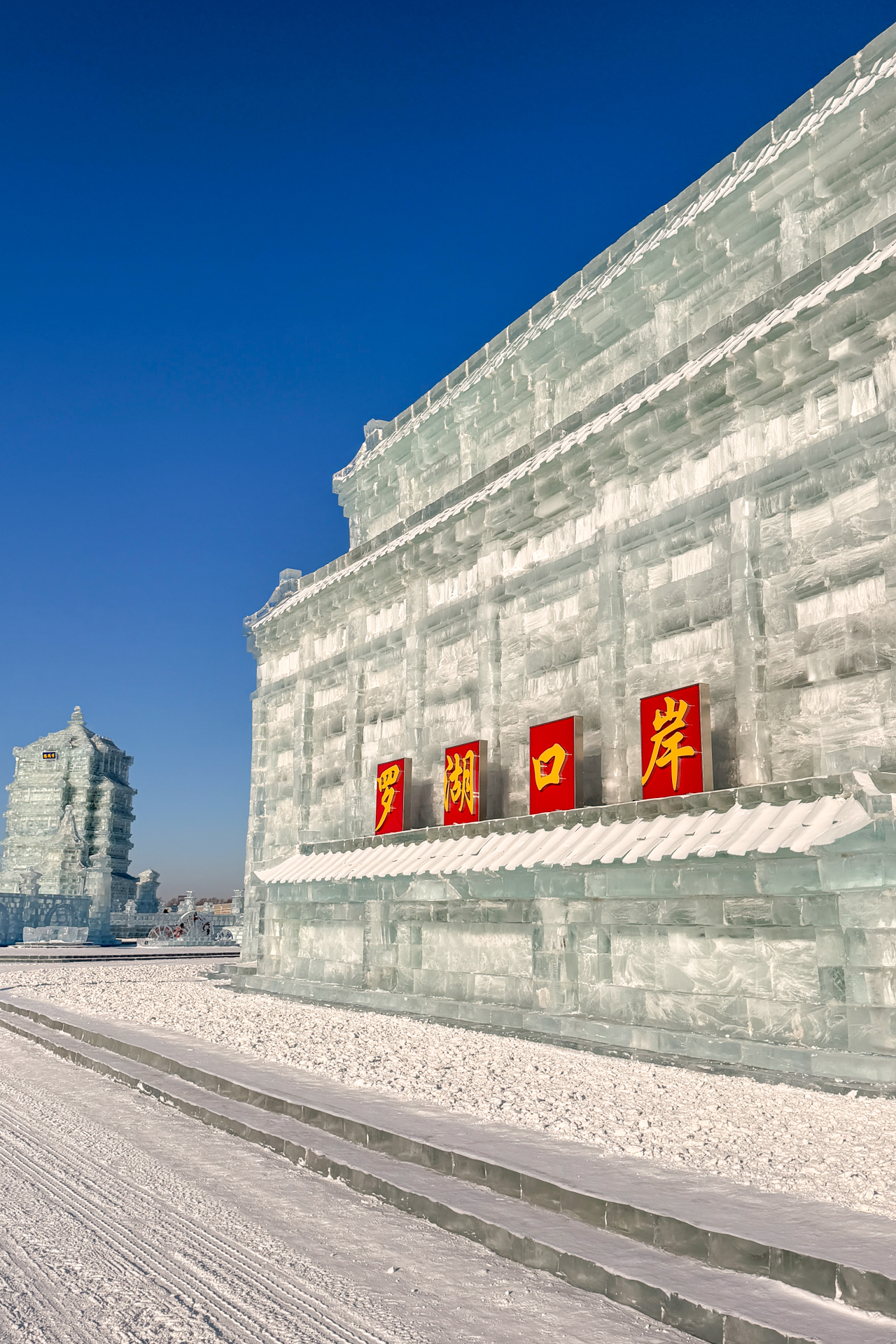 Ice wall with Chinese signs at Harbin Ice and Snow World under a clear blue sky.