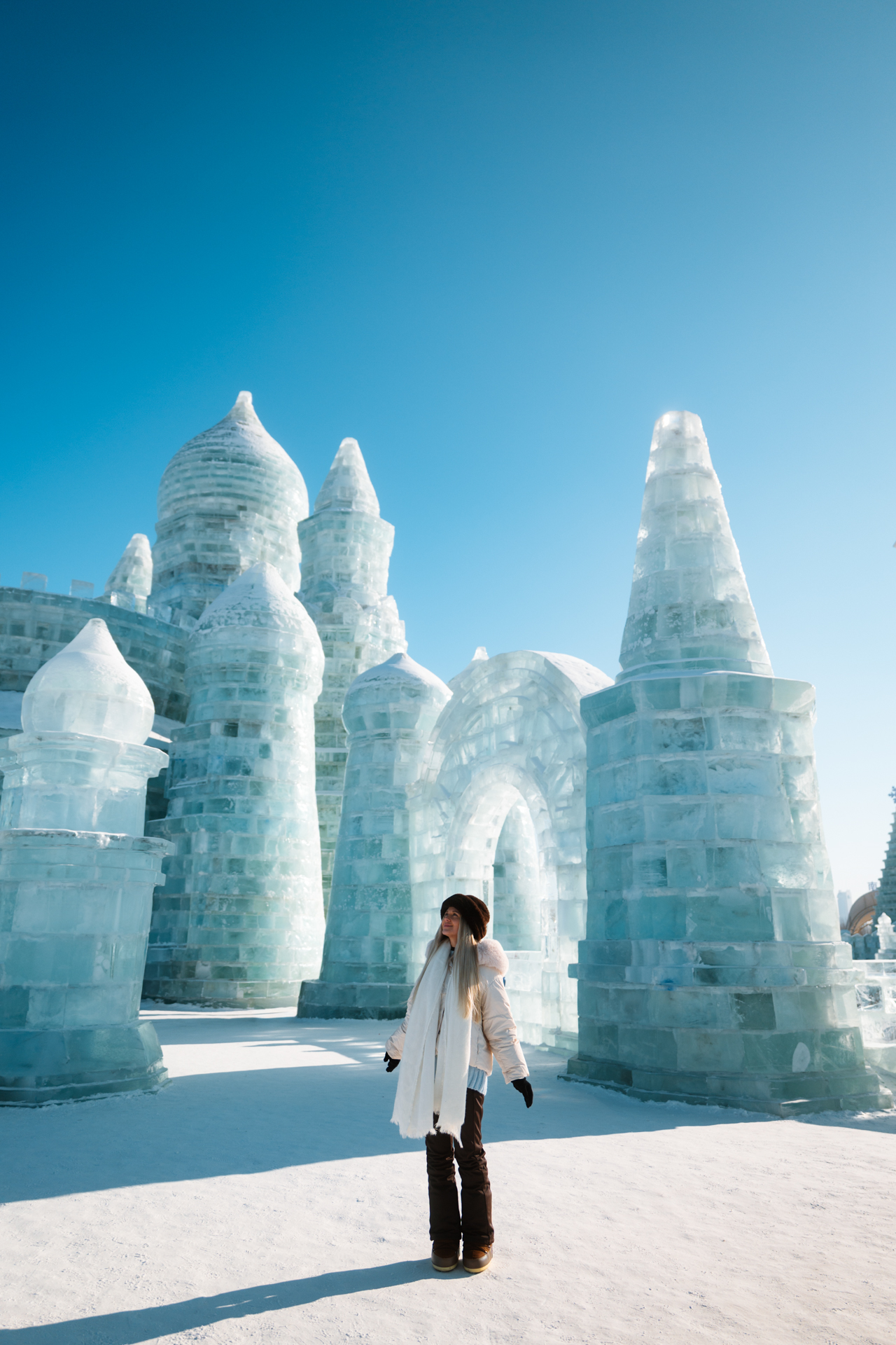 Woman standing among towering ice castle sculptures at Harbin Ice and Snow World.