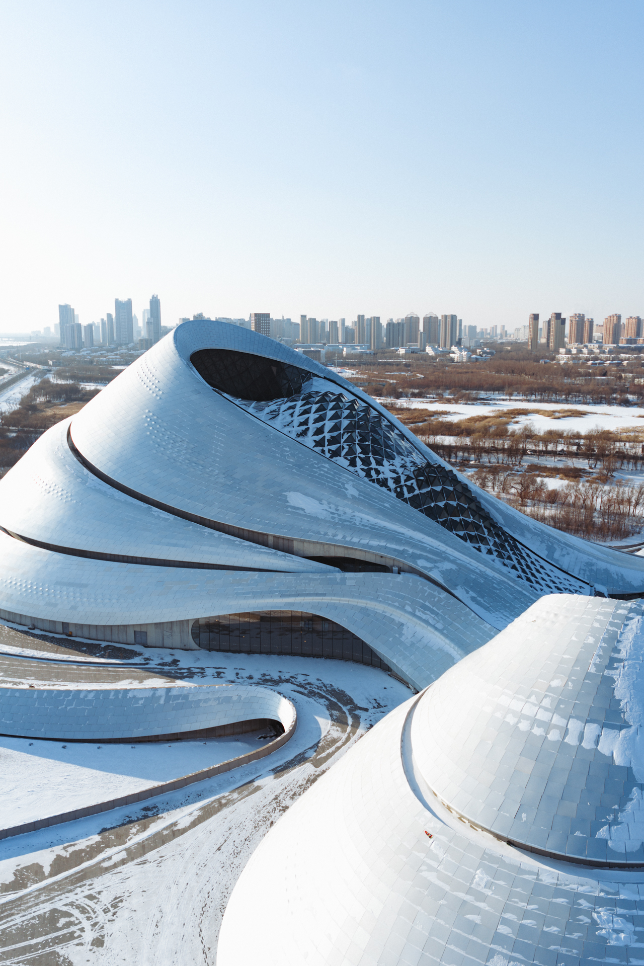 Harbin Grand Theatre surrounded by snow with the city skyline in the background.