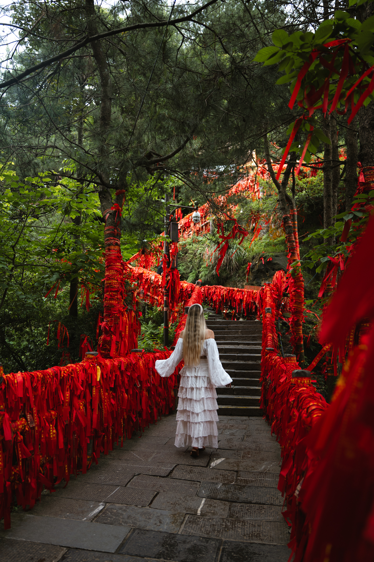 Woman walking along a forest path covered in red ribbons in Zhangjiajie, China.