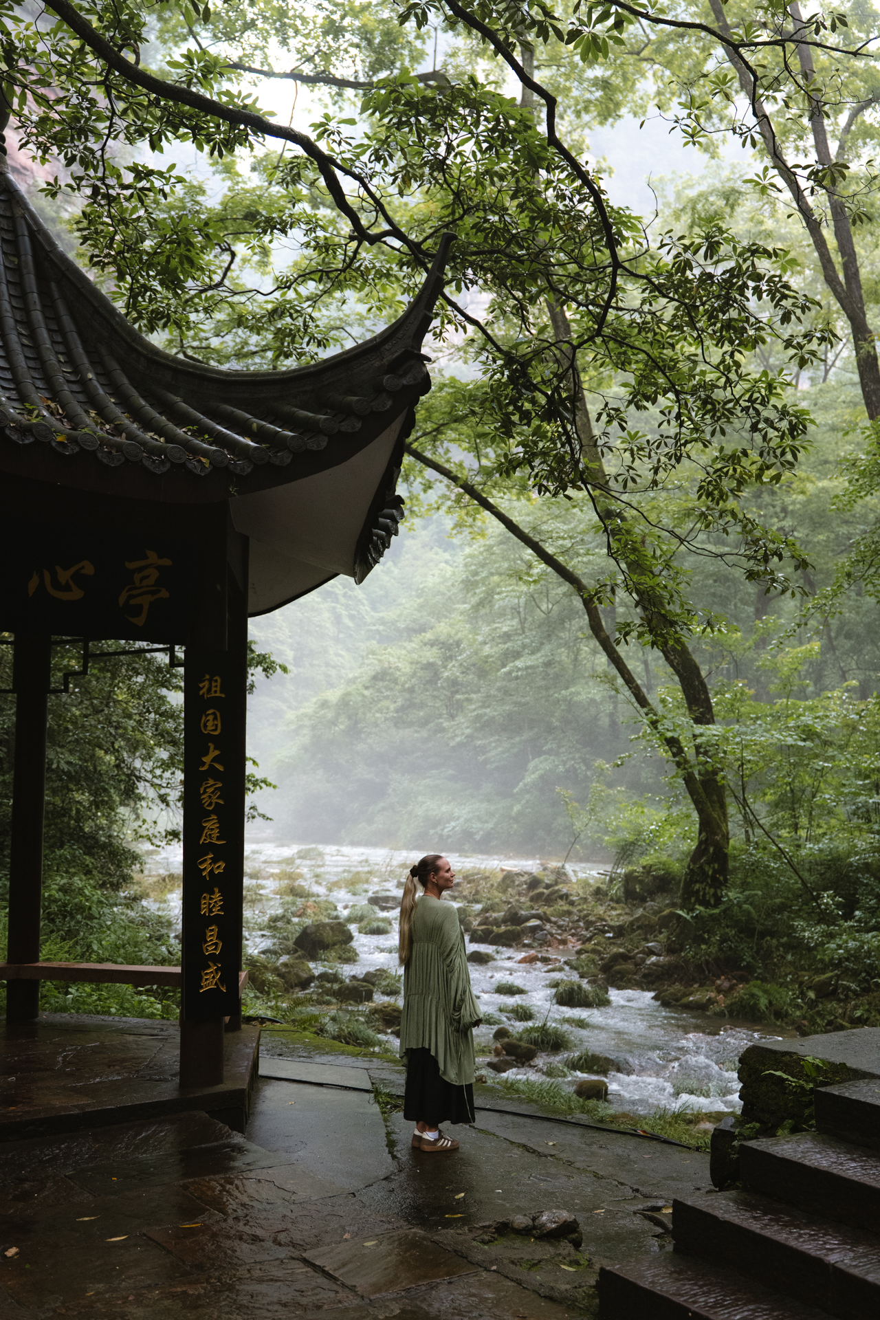 Woman beside a misty forest stream in Zhangjiajie National Forest Park, China.