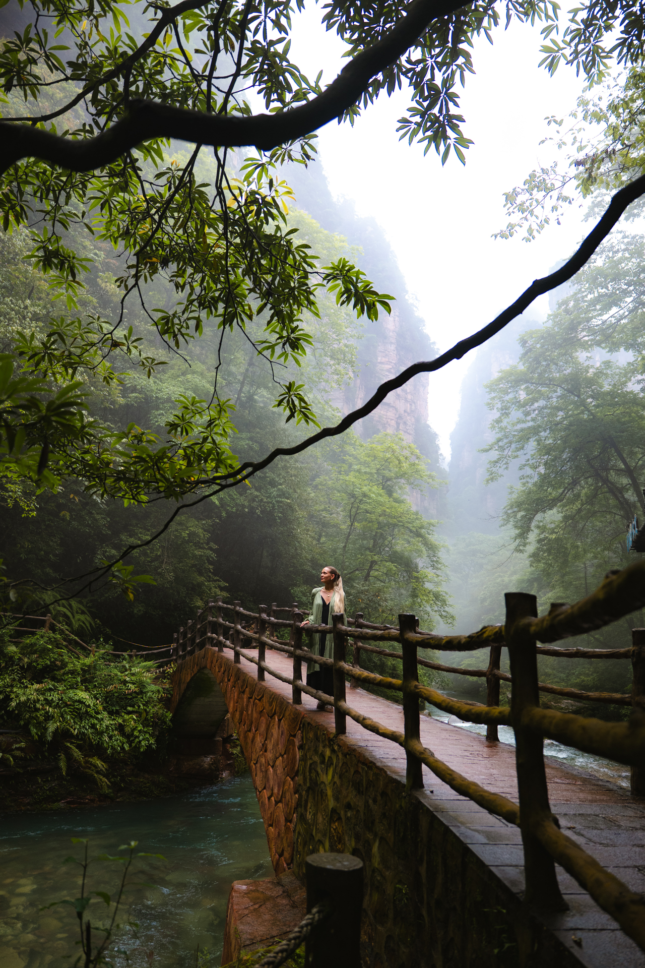 Woman standing on a stone bridge in misty Zhangjiajie National Forest Park.