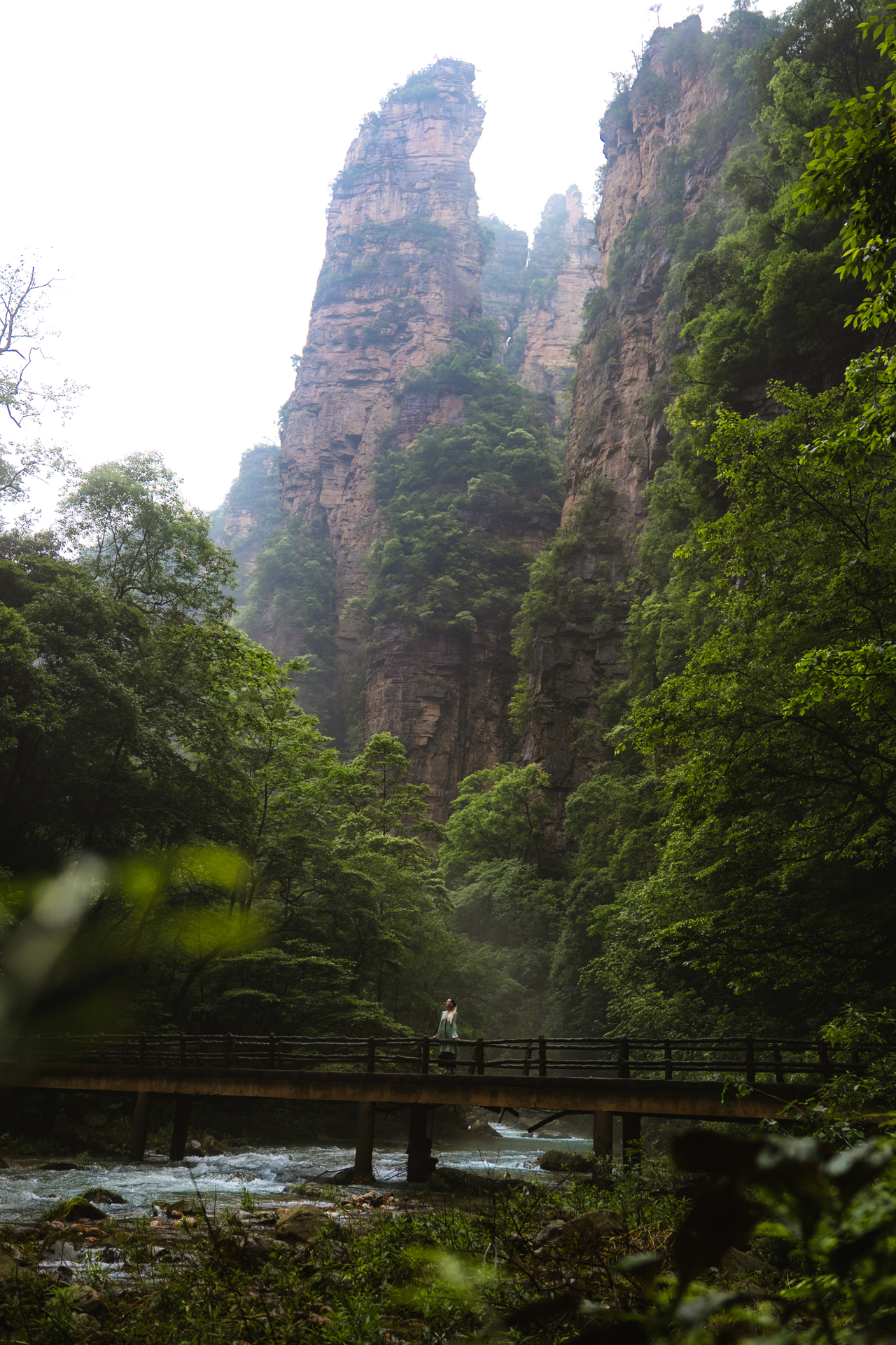 Woman standing on a bridge beneath towering sandstone cliffs in Zhangjiajie, China.