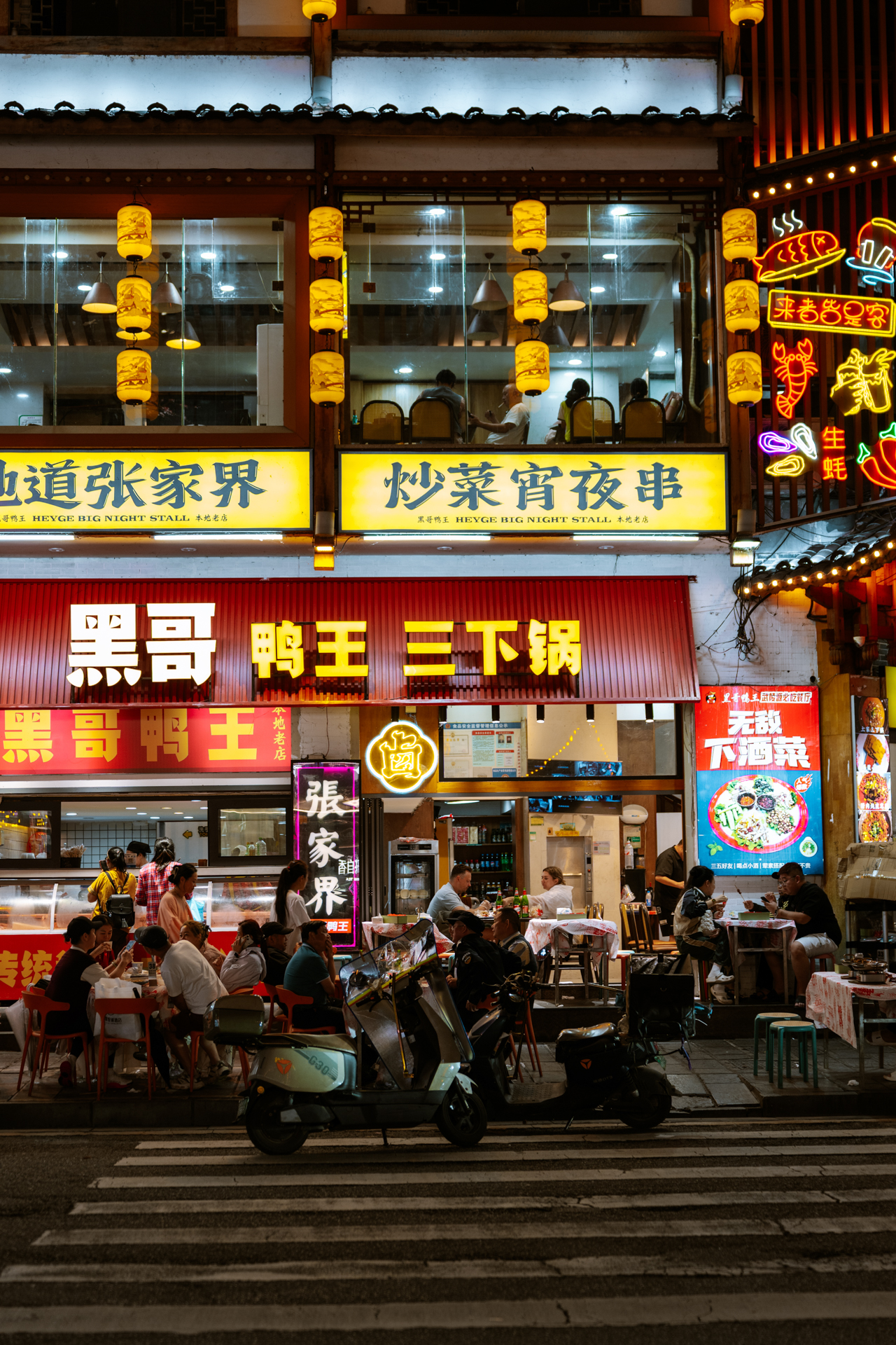 Busy night food street with local restaurants, neon signs and diners in Wulingyuan, Zhangjiajie, China.