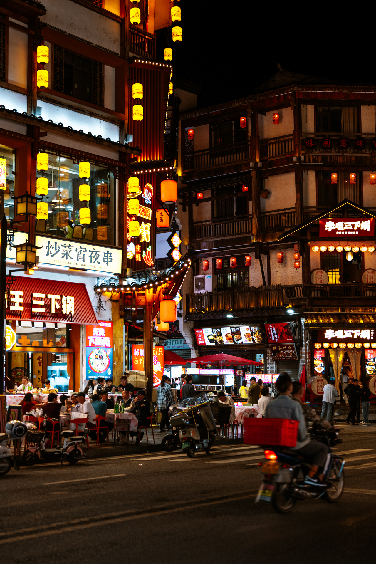 Busy restaurant street with lanterns, scooters and diners at night in Zhangjiajie, China.